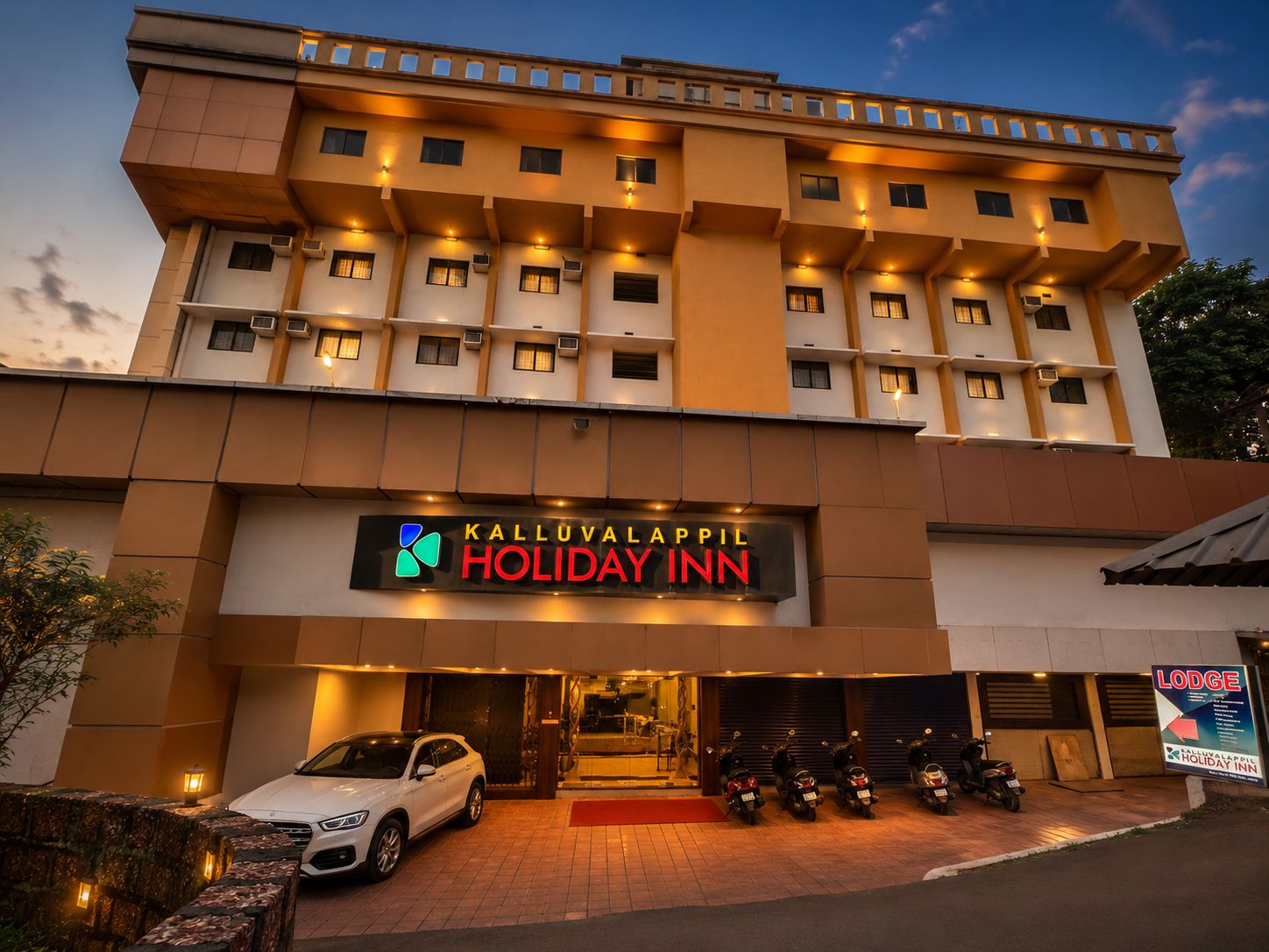 Kalluvalappil Holiday Inn exterior lit up at dusk